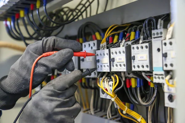 Elektrik mühendisi ana güç dağıtım panosundaki elektrik akımı voltajını kontrol etmek için dijital çoklu metre ölçüm ekipmanı kullanıyor..