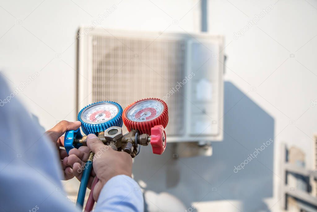 Technician using manifold gauge is measuring equipment for filling industrial factory air conditioners and checking maintenance outdoor air compressor unit.