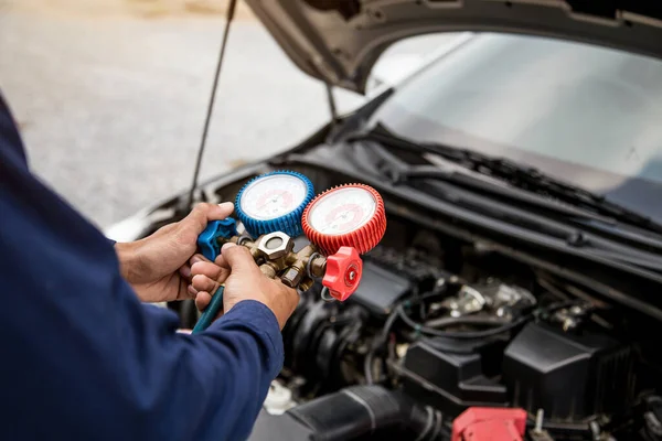 Auto mechanic using measuring equipment tool for filling car air conditioners fix checking. Concepts of car care repair service and insurance.