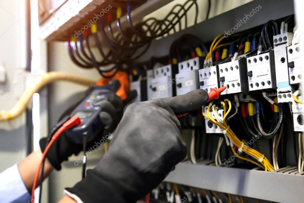 Electrical engineer using digital multi-meter measuring equipment to checking electric current voltage at circuit breaker and cable wiring system in main power distribution board.