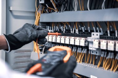 Dijital çoklu metre kullanan elektrik mühendisi, ana güç dağıtım panosundaki elektrik akımı voltajını kontrol etmek için ekipmanları ölçüyor..