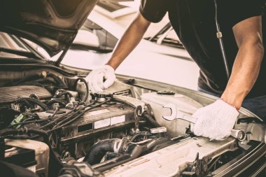 Otomobil tamircisinin yakın çekim elleri bir araba motorunu tamir etmek için ingiliz anahtarını kullanıyor. Araba bakımı onarım ve sigorta hizmetleri kavramları.