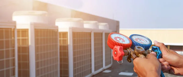 Manifold göstergesi kullanan teknisyen, açık hava kompresör ünitesini temizleyip kontrol ettikten sonra endüstriyel fabrika klimalarını doldurmak için ekipman ölçüyor..