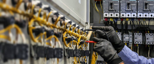 Инженер-электрик, использующий измерительное оборудование для проверки напряжения электрического тока на выключателе и кабельной проводке для технического обслуживания в главном распределительном устройстве.