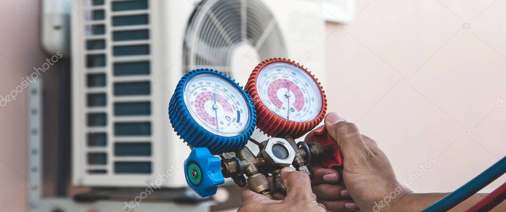 Air repair mechanic using measuring pressure gauge equipment for filling home air conditioner after cleaners and checking maintenance outdoor air compressor unit.