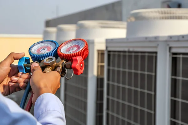 Manifold göstergesi kullanan teknisyen, açık hava kompresör ünitesini temizleyip kontrol ettikten sonra endüstriyel fabrika klimalarını doldurmak için ekipman ölçüyor..