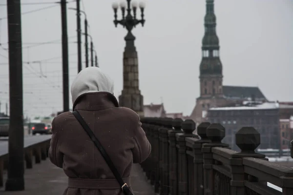 Windy winter weather. View from the back of a girl in a coat and headscarf on the bridge in Riga.