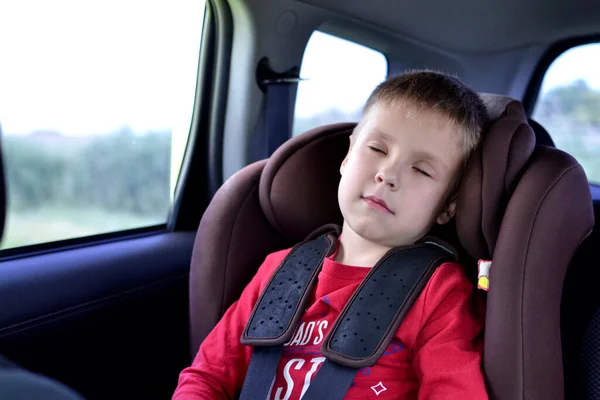 A child in a red T-shirt sleeps fastened in a car seat while traveling by car.