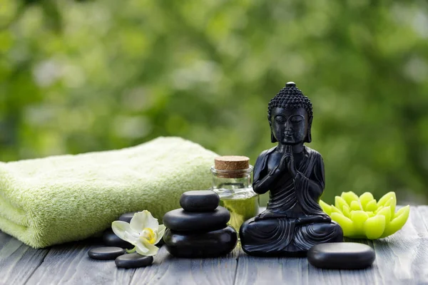 Buda heykelciği, yağ şişesi ve zen taşlarıyla kaplıca ve sağlık kompozisyonu. Banyo, masaj ve rahatlama için hazır. Kopyalama alanı ile bulanık arkaplan