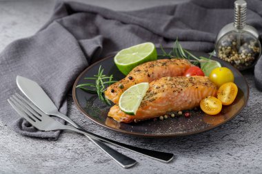 Seramik tabakta ızgara somon bifteği, sebze, limon ve baharat. Tabak bir taş masada servis edilir.