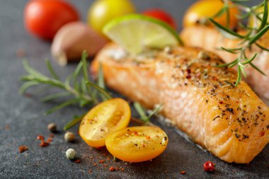 Izgara somon bifteği, domates, sebze, kireç ve baharatlı taş tahtada. Seçici odak