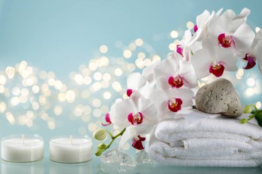 Orkide, iki mum ve mavi arka planda havlu ile kış spa süslemesi ve çözünmüş çelenk ışıkları.