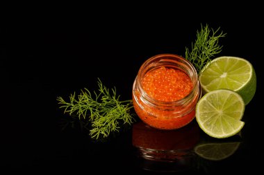 Cam bir kavanozda kırmızı somon balığı havyarı, limon ve dereotu siyah arka planda.. 