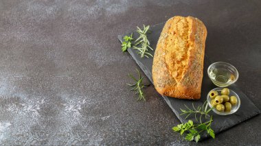 Taze pişmiş İtalyan Ciabatta 'sı. Taş tahtada otlar, baharatlar ve zeytinlerle birlikte.. 