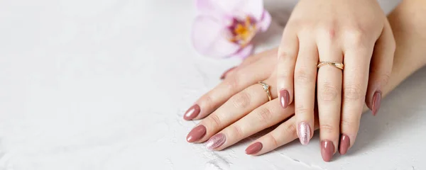 Taze manikürlü güzel eller bir orkide çiçeğinin yanında beyaz bir taş tahtanın üzerinde yatıyor. Spa ya da sağlık pankartı