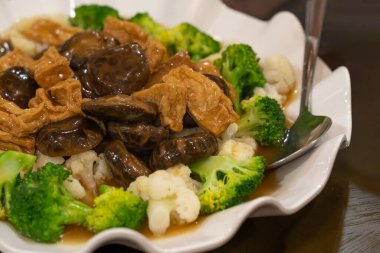 Taze mantarlı baharatlı vejetaryen yemeği, buharda pişirilmiş brokoli, karnabahar ve lezzetli bir sosta servis edilen soya fasulyesi bazlı malzemeler..