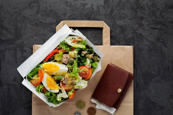 Nicoise salad with tuna in paper box on dark background flat lay.Take away of natural organic meals.Healthy food and diet concept.Delivery service of restaurant food of high quality