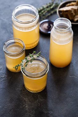 Koyu gri arka plan manzaralı sarı taze kemik suyuna bulanmış cam kavanoz. Sağlıklı düşük kalorili yiyecekler vitamin, kolajen ve iltihaplı amino asit açısından zengindir.
