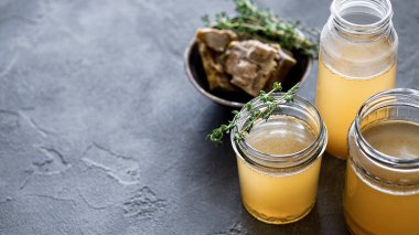 Koyu gri arka planda sarı taze kemik suyuyla cam kavanoz. Sağlıklı düşük kalorili yiyecekler vitamin, kolajen ve iltihaplı amino asit açısından zengindir.
