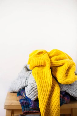 Ahşap masaya örülmüş renkli yün ya da süveter yığınları ve kopya alanla yakın plan beyaz duvar. Akraba bağışı ve ev konsepti.