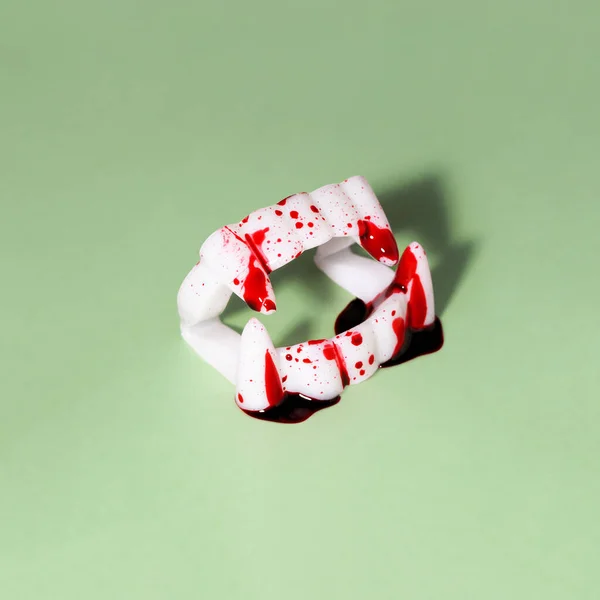 Vampire Dracula toy teeth with blood on green background. Creative Halloween minimal concept