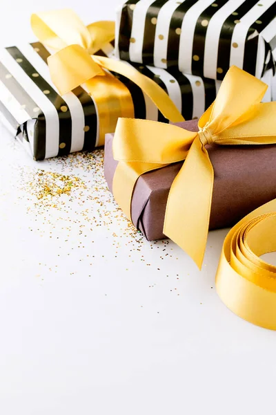 Wrapped gifts in black and white,purple paper,golden ribbon on golden sparkles white background with copy space.Preparation for celebrate concept