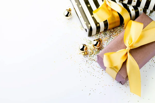 Wrapped gifts in black and white,purple paper,golden ribbon and festive decoration on golden sparkles white background with copy space top view,flat lay.Template mockup greeting card text design