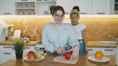Avrupalı bir kadın ve Afrikalı bir kız mutfakta kırmızı ve sarı biberli salata hazırlıyorlar. Kız annesinin sebzeleri dilimleyişini hevesle izliyor. Yemek pişirme ya da ev eğlencesi kavramı