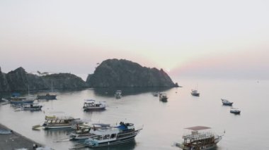 Okyanustaki dağlardan gün doğumu veya gün batımı, doğal manzara, pembe gökyüzü, balıkçı tekneleri ve turist gemileri, denizde yatlar, insansız hava aracı görüntüsü, Türkiye 'deki körfezin panoramik manzarası.