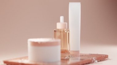 Yüz ve vücut derisi için kozmetik ürünler. Serum için pipetli cam şişe ve kahverengi masasında tuba olan plastik kavanozlar. Bej arkaplandaki boş beyaz paketler buzlu bir su spreyinde.