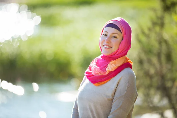 Attractive confident woman in hijab standing outdoors in sunny summer day, happily smiling. Muslim woman lifestyle concept