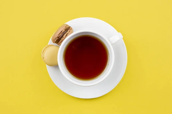 French colorful macaroons dessert and a cup of tea on a yellow background. Top view.