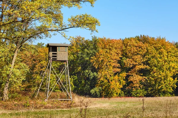 Wooden elevated deer hunting blind at the edge of a forest and field.