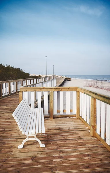 Empty bench on a wooden boardwalk by a beach — Stock Photo, Image