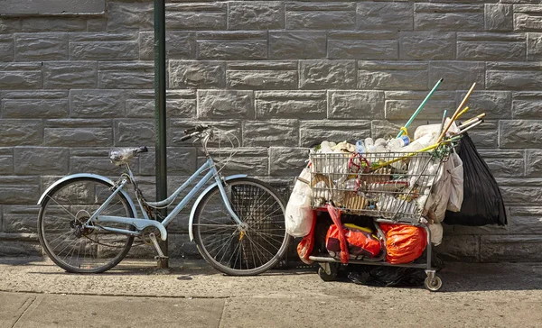 Cykel och kundvagn fylld med skräp på en gata. — Stockfoto