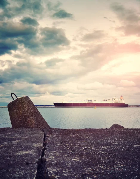 Concrete breakwater with a LNG tanker in distance at sunset. — Stock Photo, Image