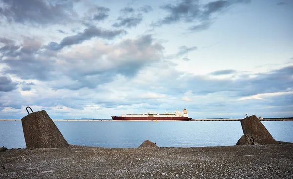 Concrete breakwater with a LNG tanker in distance at sunset — Stock Photo, Image