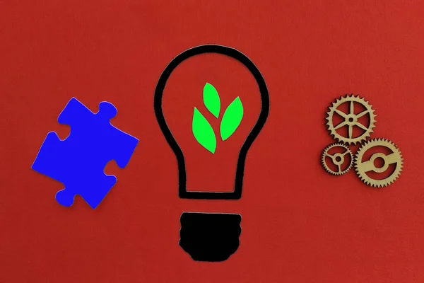 Electric light bulb with plant leaves, wooden gears, puzzle on a red background. Creativity, Creative ideas.