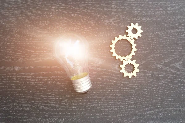 Electric light bulb, wooden gears on a dark background. Business ideas, creativity.