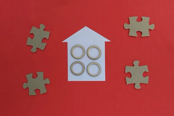 House, wooden gears, cardboard puzzles on a red background. Realty. Housing market.