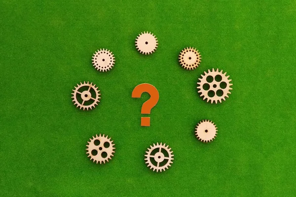 Question mark, wooden gears on a green background. Problem solving, thinking, and ideas.