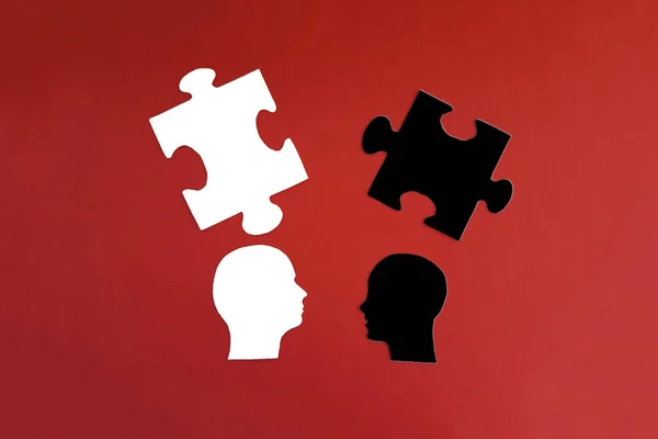 Two human heads, a pair of white and black puzzles on a red background. The concept of communication, mental interaction. Collective thinking.