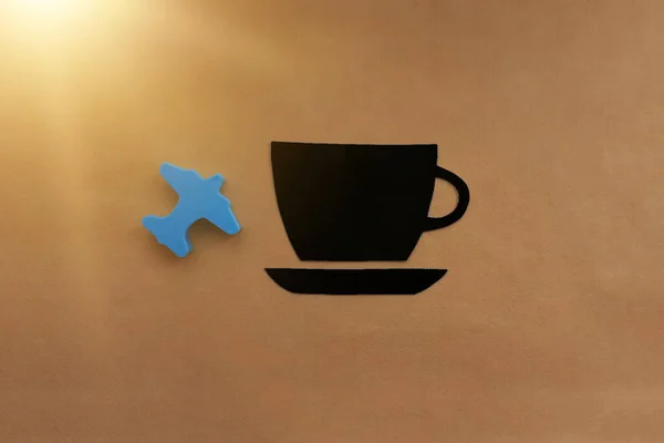 A Cup of coffee is black, a plane is blue on a light brown background. Morning flight, travel.