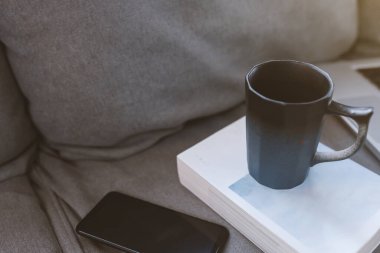 Oturma odasındaki koltukta cep telefonlu bir fincan kahve..