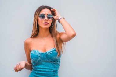 Yaşam tarzı oturumu, mavi kot elbiseli beyaz tenli genç bir esmer ve gri arka planda güneş gözlüğü, kopyalama ve yapıştırma için yer var.