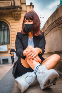 Streetstyle, a young brunette with a mask on her face from the coronavirus pandemic, sitting in the city thinking things. Lack of confidence after the covid-19, social distance clipart