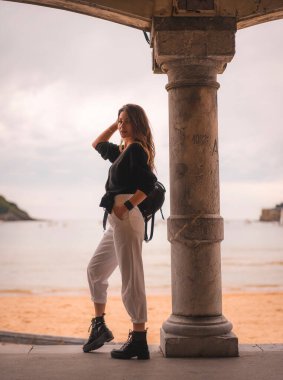 Şehirde beyaz pantolonlu sarışın bir kız ve plaja yakın deri ceketli bir kız. Sahilin sığ kesimlerinde kolları saçlarında bir sütunun yanında fotoğraflar.