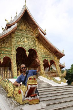 Luang Prabang 'daki Wat Ho Pha Bang tapınağına karşı poz veren adam Laos' u cepheden gördü.