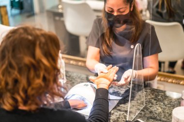 Manikür ve pedikür salonu, koronavirüs, covid-19, sosyal mesafe. Salgın nedeniyle yeniden açılması, güvenlik önlemleri. Manikür yaptırdıktan sonra eline masaj yapan bir kadın işçi.