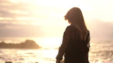 Genç adam arka planda güneş varken denizde yürüyor ve dans ediyor. Deniz kenarında gün batımında şeffaflığı olan uzun siyah elbiseli esmer bir kadının yaşam tarzı..